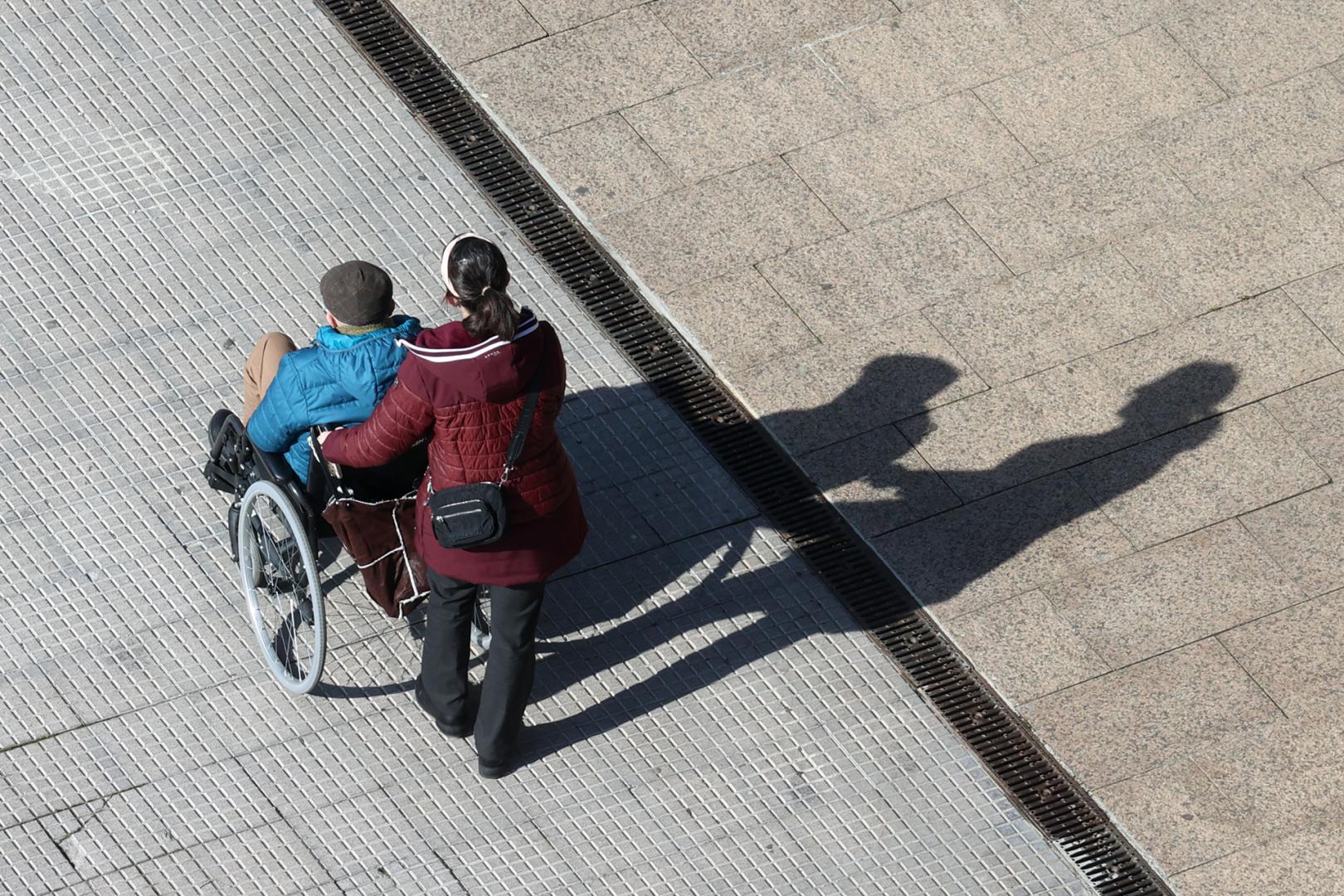 Una mujer pasea a una persona en silla de ruedas.