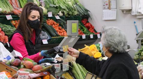 Una persona mayor entrega una tarjeta a la dependienta de una frutería para pagar la compra recién realizada en un puesto del mercado del Ensanche Una persona mayor entrega una tarjeta a la dependienta de una frutería para pagar la compra recién realizada en un puesto del mercado del Ensanche