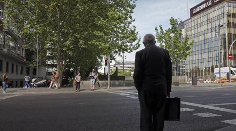 Un hombre aguarda con su maletín a que se abra el semáforo para cruzar una calle. Un hombre aguarda con su maletín a que se abra el semáforo para cruzar una calle.