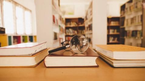 Imagen de una lupa y unas gafas sobre unos libros en la biblioteca Imagen de una lupa y unas gafas sobre unos libros en la biblioteca