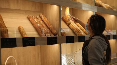 Una trabajadora de la tienda de Ogipan en la Plaza San Francisco de Pamplona selecciona con la pinza una barra de pan para servirla a un cliente. Una trabajadora de la tienda de Ogipan en la Plaza San Francisco de Pamplona selecciona con la pinza una barra de pan para servirla a un cliente.
