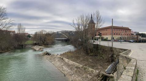 Viandantes por el puente de Santa Engracia, con el azud del mismo nombre en el río y partido por la mitad Viandantes por el puente de Santa Engracia, con el azud del mismo nombre en el río y partido por la mitad