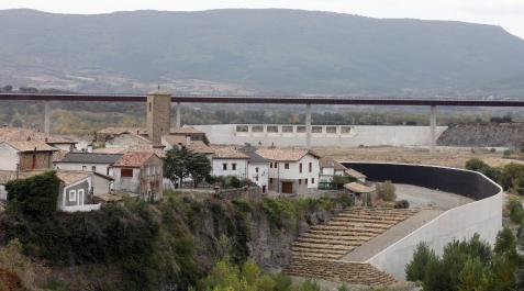 RODEADOS POR OBRAS Casco urbano de Sigüés (Aragón) con el muro de protección para el pueblo en primer plano y, al fondo, el dique de cola del embalse de Yesa, ambos en obras. Arriba, el viaducto ya en servicio de un tramo de la A-21 del que partirá el fut RODEADOS POR OBRAS Casco urbano de Sigüés (Aragón) con el muro de protección para el pueblo en primer plano y, al fondo, el dique de cola del embalse de Yesa, ambos en obras. Arriba, el viaducto ya en servicio de un tramo de la A-21 del que partirá el futuro acceso a Sigüés que conducirá asimismo hacia el valle de Roncal.
