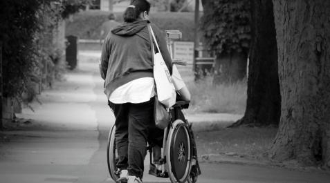 cuidadora-dependencia Una cuidadora empuja a una persona en silla de ruedas