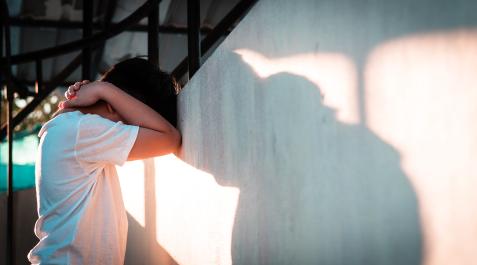 JovenesSaluMental Un joven se apoya contra una pared tapándose el rostro con los brazos.
