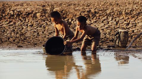 Niños agua Dos niños juegan con un cubo en la orilla de un río.