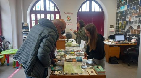 Punto de información del Consorcio Turístico de Tierra Estella Nerea Tardienta, de prácticas en el Consorcio Turístico de Tierra Estella, atiende a dos turistas en el punto de información de la entidad. Al fondo, la técnico del consorcio, Garbiñe García San Martín