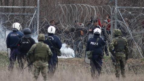 Un grupo de migrantes intenta de cruzar la frontera griega, mientras la policía trata de evitarlo lanzando botes de gases lacrimógenos