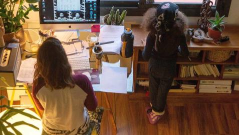 Una mujer realiza teletrabajo en su casa mientras su hija juega a su lado