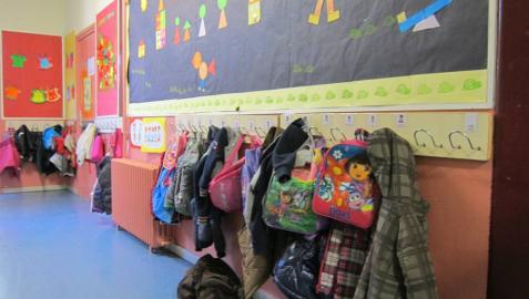 Mochilas y ropa en el perchero de un aula infantil.