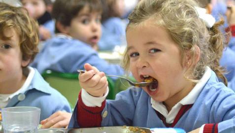Una niña, en un comedor escolar, se lleva la comida a la boca. Una niña, en un comedor escolar, se lleva la comida a la boca.