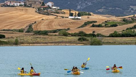 Alumnos de la Escuela Navarra de Vela practican piragüismo en el embalse de Alloz con Villanueva de Yerri de fondo. Fotografía de archivo del 22 de agosto de 2020
