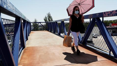 Una mujer con mascarilla se protege del sol cuando cruza por una pasarela en Madrid