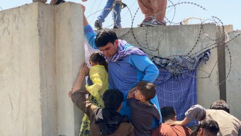 Un padre ayuda a sus hijos a superar un muro para entrar en el aeropuerto de Kabul