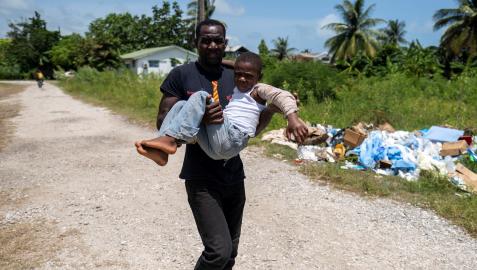 Hombre carga a un niño herido hacia un centro medico para que reciba tratamiento en Les Cayes