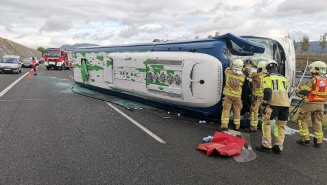 Bomberos atienden a los afectados en el accidente con un autobús volcado.