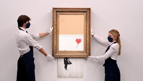 Empleados de la galería muestran la obra de Banksy 'Love is in the Bin'