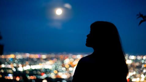 LunaLlena Una joven observa una ciudad con la luna llena al fondo