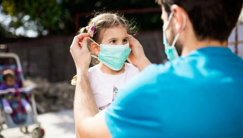 Un padre coloca una mascarilla a una niña Un padre coloca una mascarilla a una niña