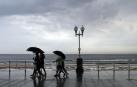 Varias personas se protegen con el paraguas de la lluvia, en el paseo de muro de la playa de San Lorenzo de Gijón
