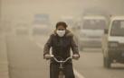 Joven china, protegida por una mascarilla, circula en bicicleta por una calle de Lanzhou, ciudad que sufre unos niveles altos de contaminación.