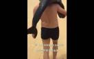 Graban a un hombre con un delfín al hombro paseando por una playa china