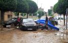Varios jóvenes intentan desatrapar un coche en una calle de Olite totalmente embarrada con la torre del castillo, al fondo.