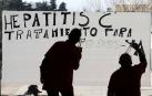 Dos personas teminan de pintar un cartel sobre un cristal en el Complejo Hospitalario de Navarra en favor del tratamiento de la Hepatitis C.
