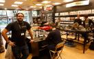 Carlos Miguélez, junto a un cliente en la mesa de decoración. A la derecha tres jóvenes juegan en un escenario.