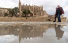 Dos viandantes pasan junto a un charco cerca de la catedral de Palma de Mallorca.