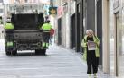 Una mujer regresa de comprar el pan y la prensa en Pamplona. Al fondo, el servicio de recogida de basuras, que sigue funcionando.