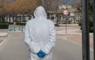 Una persona con un traje de protección, frente un cementerio.