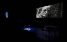 Fotograma del filme que recoge una imagen del concierto homenaje con una banqueta vacía en el escenario y un autorretrato de Aute proyectado.