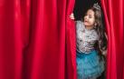 Imagen de una niña tras el telón en un escenario de teatro