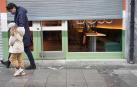 Un hombre y una niña pasan por delante de un establecimiento cerrado en Bilbao.