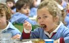 Una niña, en un comedor escolar, se lleva la comida a la boca.