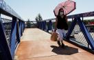 Una mujer con mascarilla se protege del sol cuando cruza por una pasarela en Madrid