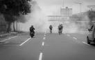 Varias personas circulan en moto o bicicleta entre el humo en una ciudad