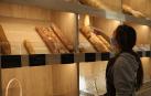 Una trabajadora de la tienda de Ogipan en la Plaza San Francisco de Pamplona selecciona con la pinza una barra de pan para servirla a un cliente.