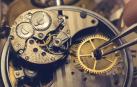 Una mano con pinzas manipula las piezas minúsculas de un reloj antiguo.