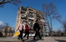 Varias personas pasan frente a un edificio de apartamentos arrasado