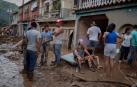 Los vecinos descansan tras trabajar para quitar toda la tierra que entró a sus viviendas dañadas por las lluvias