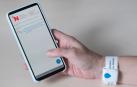 Imagen de la pulsera de geolocalización para el paciente y de la aplicación “Virtual Waiting Room” para el teléfono del acompañante