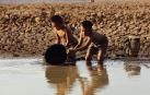 Dos niños juegan con un cubo en la orilla de un río.