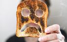 Una persona sujeta una tostada de pan de molde quemada con una cara triste./