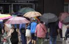 Varias personas despliegan paraguas en una calle de Gijón este mes de agosto