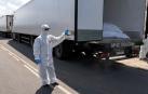 Un oficial con traje de protección contra materiales peligrosos abriendo un camión, parte de un convoy con 1.212 cadáveres de militares ucranianos fallecidos para ser repatriados