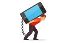 Bended man carrying on his back big and heavy mobile phone chained with shackles to his leg. Modern technology burden concept. Flat style vector illustration isolated on white background.