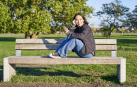 Una joven sentada en un banco tomando el sol con el móvil en la mano