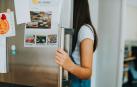 Imagen de una joven que abre la puerta de la nevera, con imanes pegados